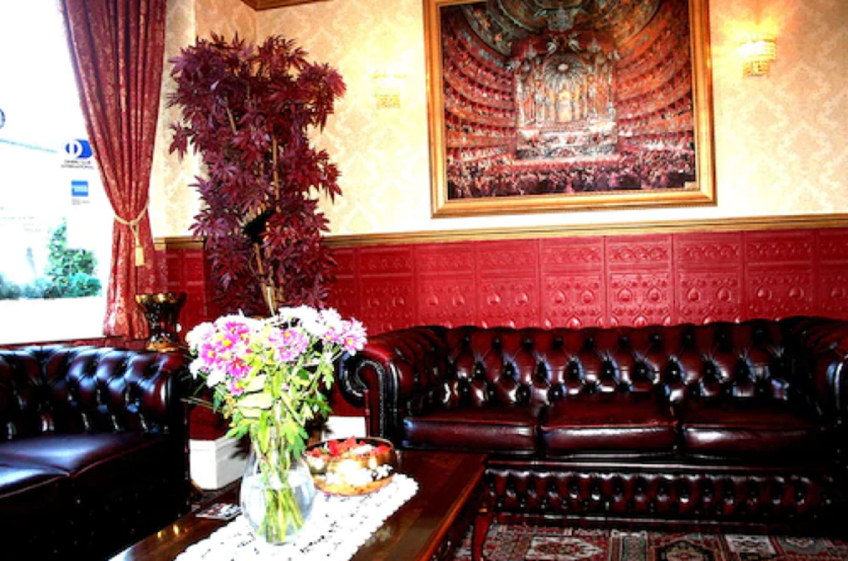 Un canapé rouge recouvert de tissu, un vase rempli de fleurs et un tableau encadré accroché au mur.