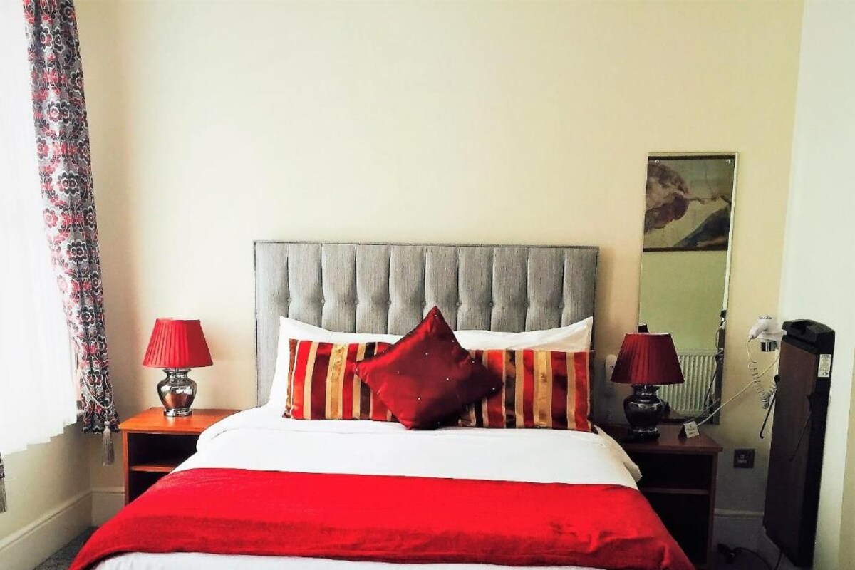 Een hotelkamer met een bed, twee nachtkastjes, een rode lamp op elk, een spiegel en een telefoon.
