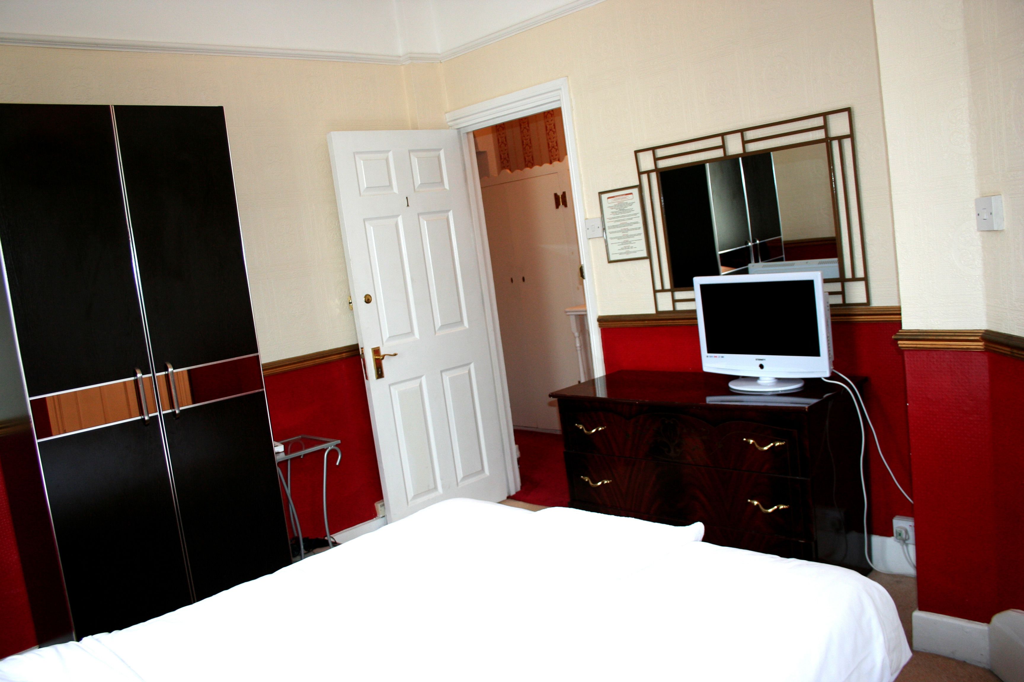 Una habitación de hotel con una cama, un aparador con televisor, un armario y una puerta que da a otra habitación.