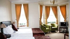 Een hotelkamer met een groot bed, twee fauteuils, een televisie en gordijnen.