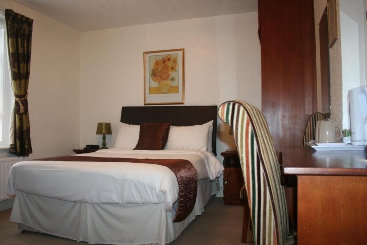 Een hotelkamer met een groot bed, een bureau, een stoel, een lamp en een schilderij aan de muur.