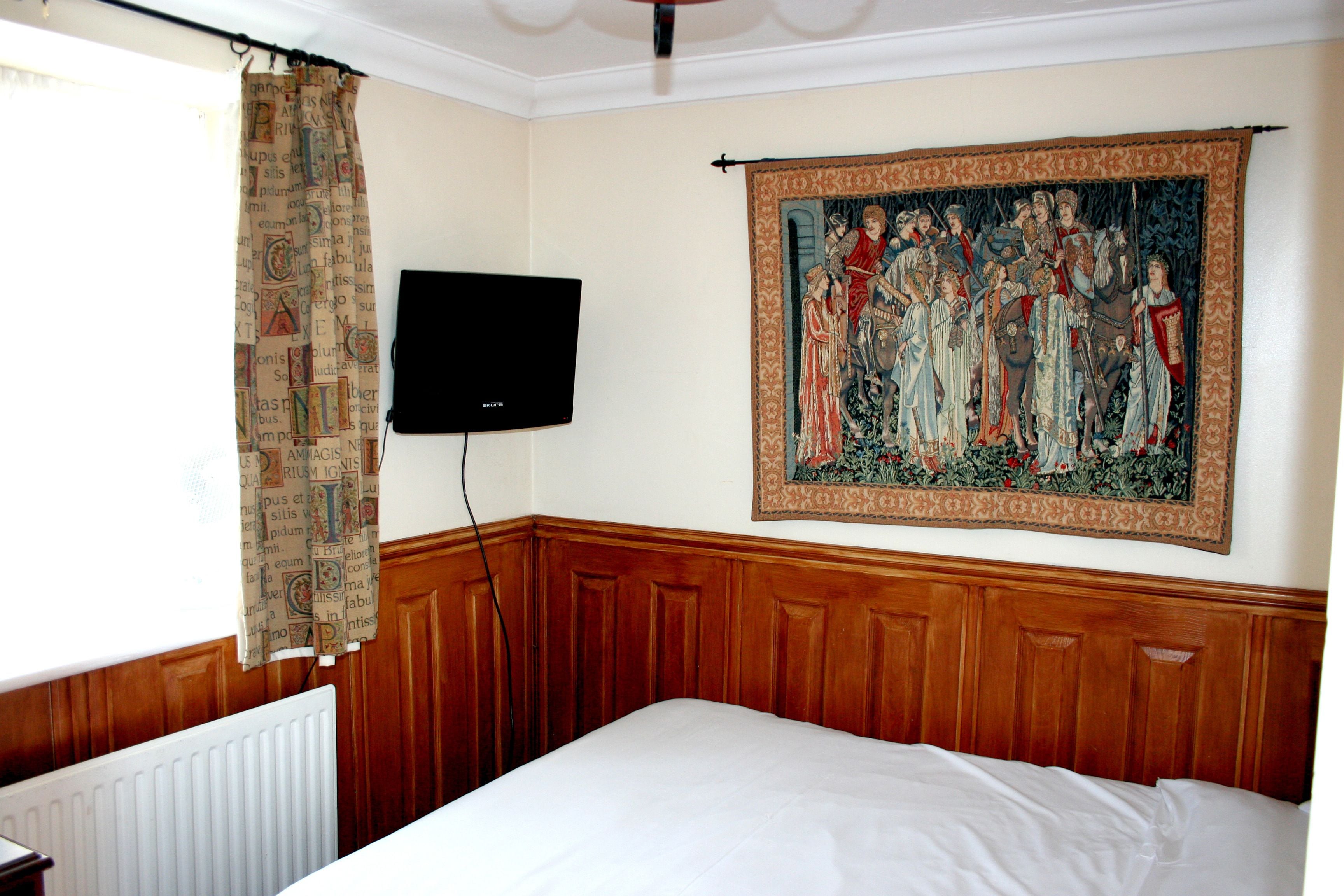 Een slaapkamer met een groot bed, een flatscreen televisie aan de muur en een wandtapijt met afbeeldingen van historische figuren.