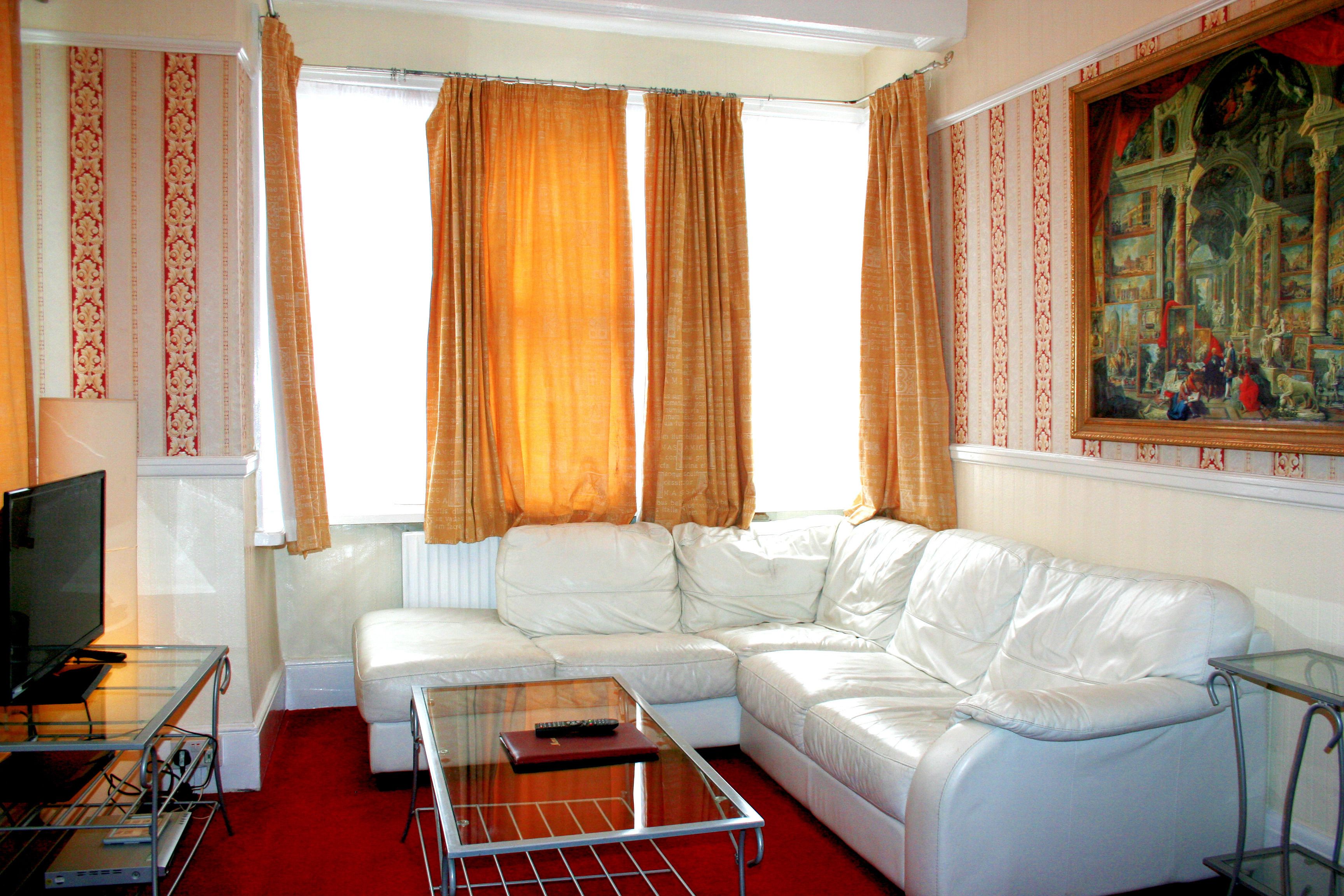 A living room with a white leather sofa, a glass coffee table, a television, and a painting on the wall.