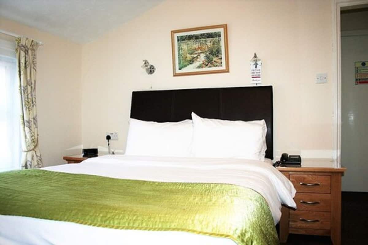 Een hotelkamer met een bed, nachtkastje, lamp, een lijst met een foto aan de muur en een deur.