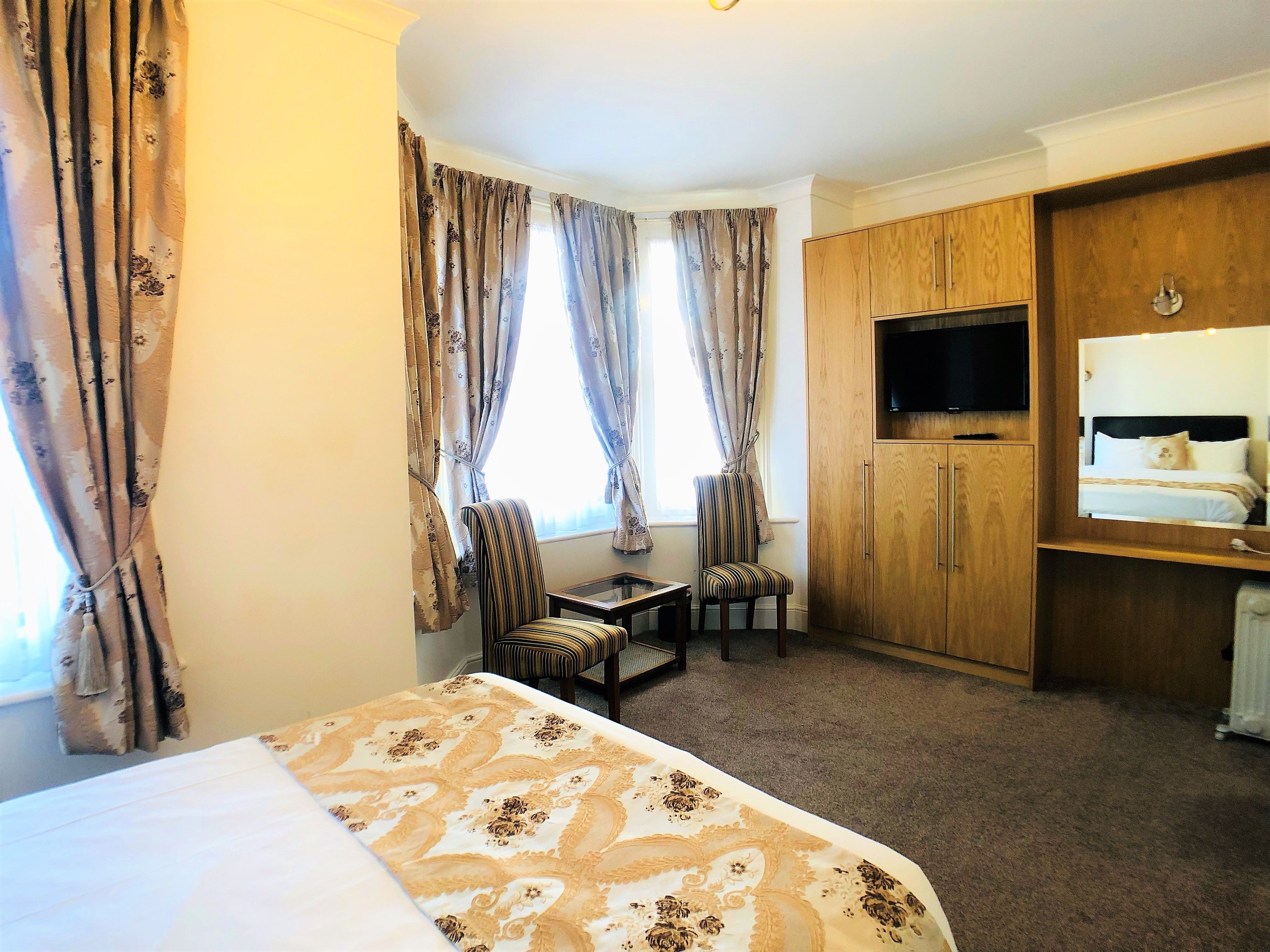 Una camera d'albergo con un letto, una scrivania, due sedie, una televisione e un armadio.