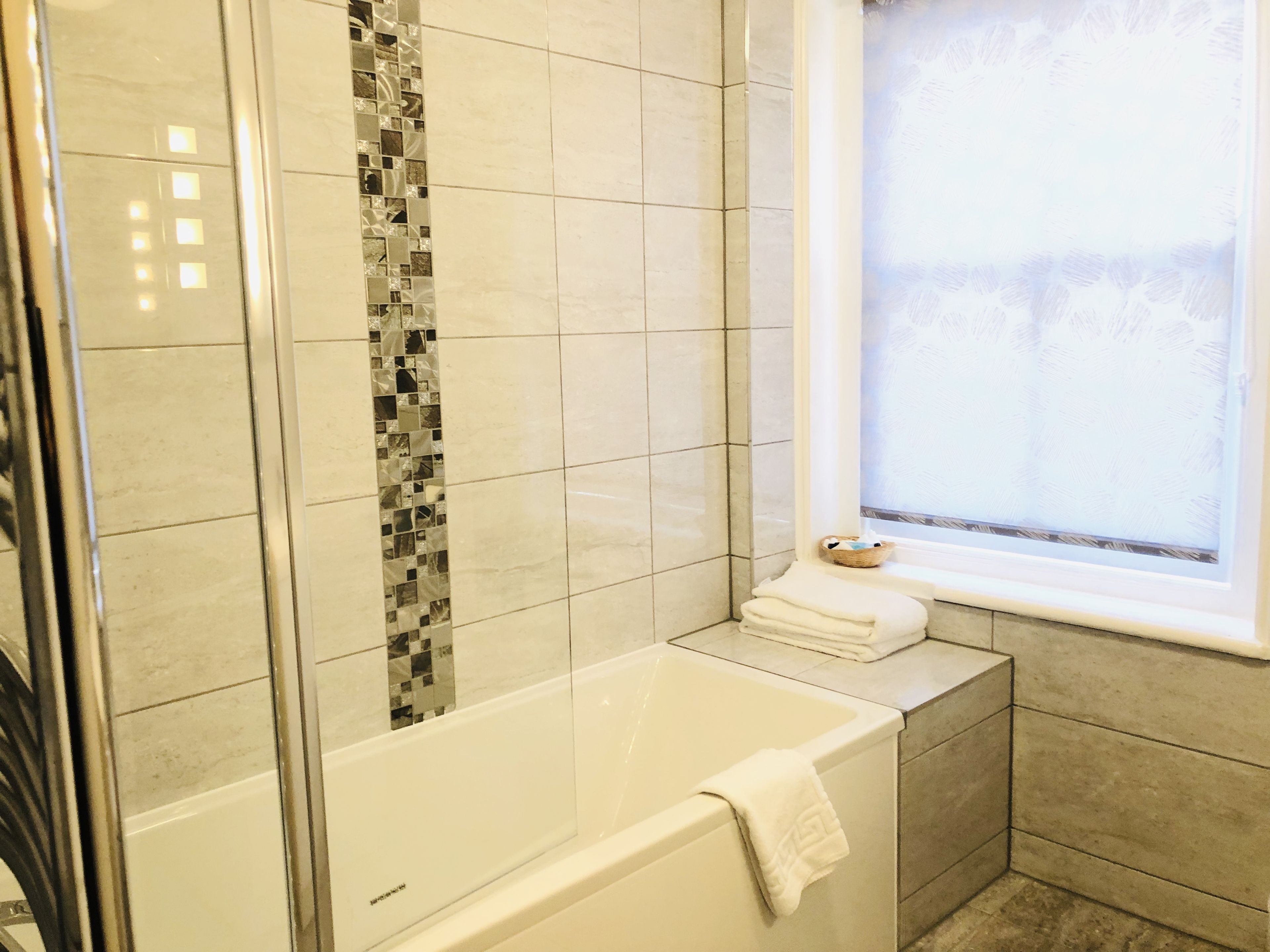 A modern bathroom with a glass shower enclosure, a white bathtub, and a window with frosted glass.