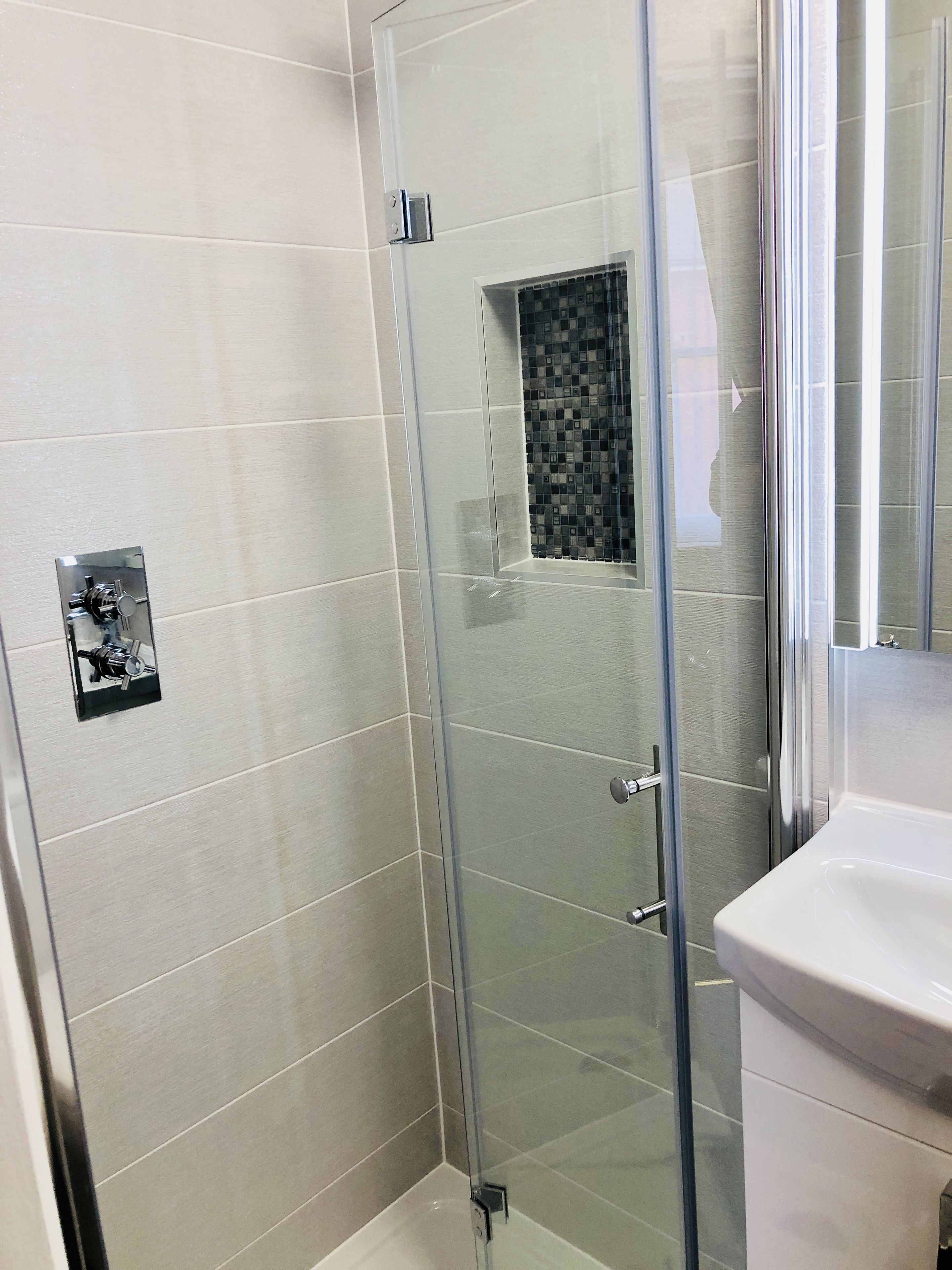 A bathroom with a glass-enclosed shower, a white sink, and a tiled floor.