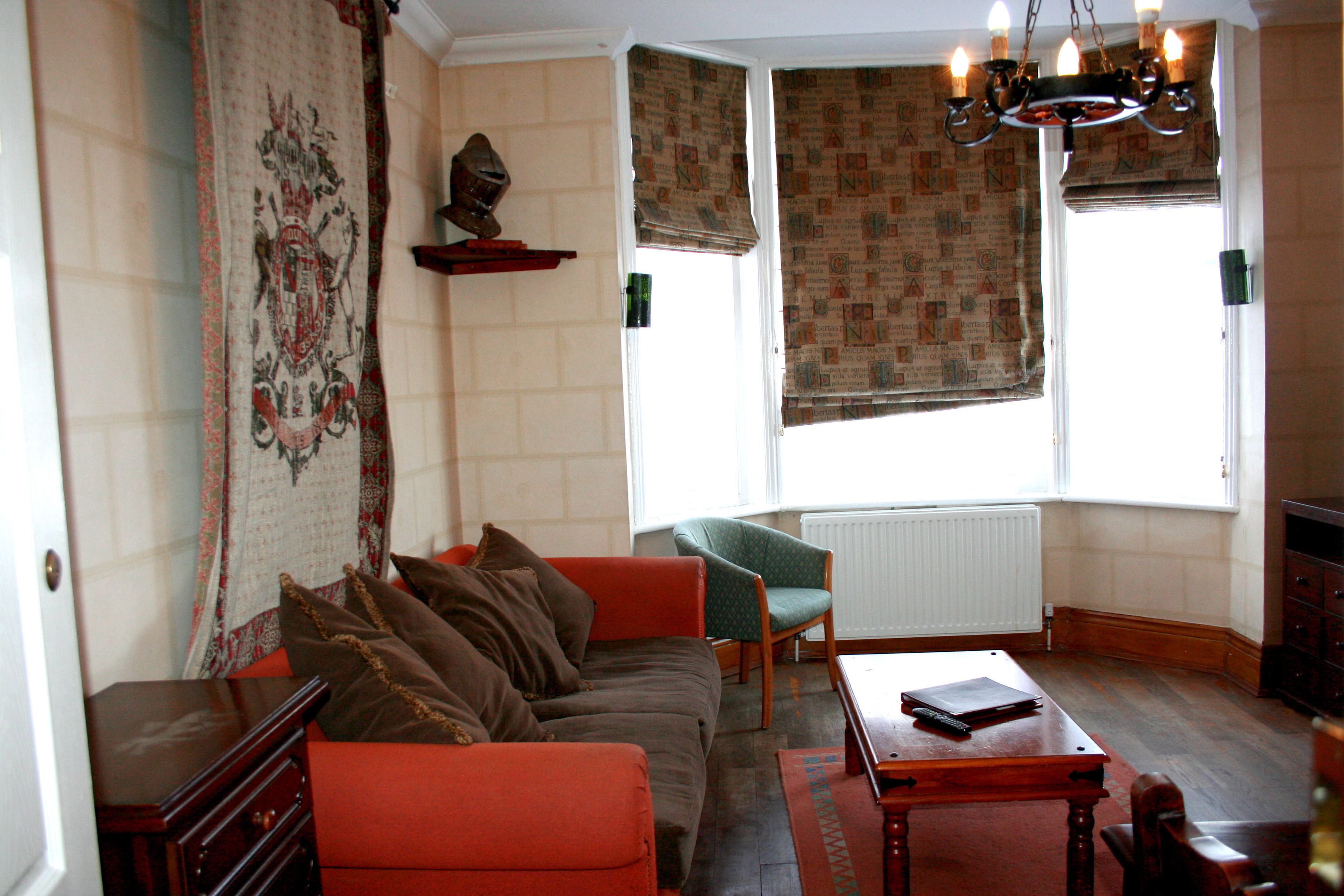 Een woonkamer met een bank, fauteuil en een tafel met een boek en afstandsbediening.