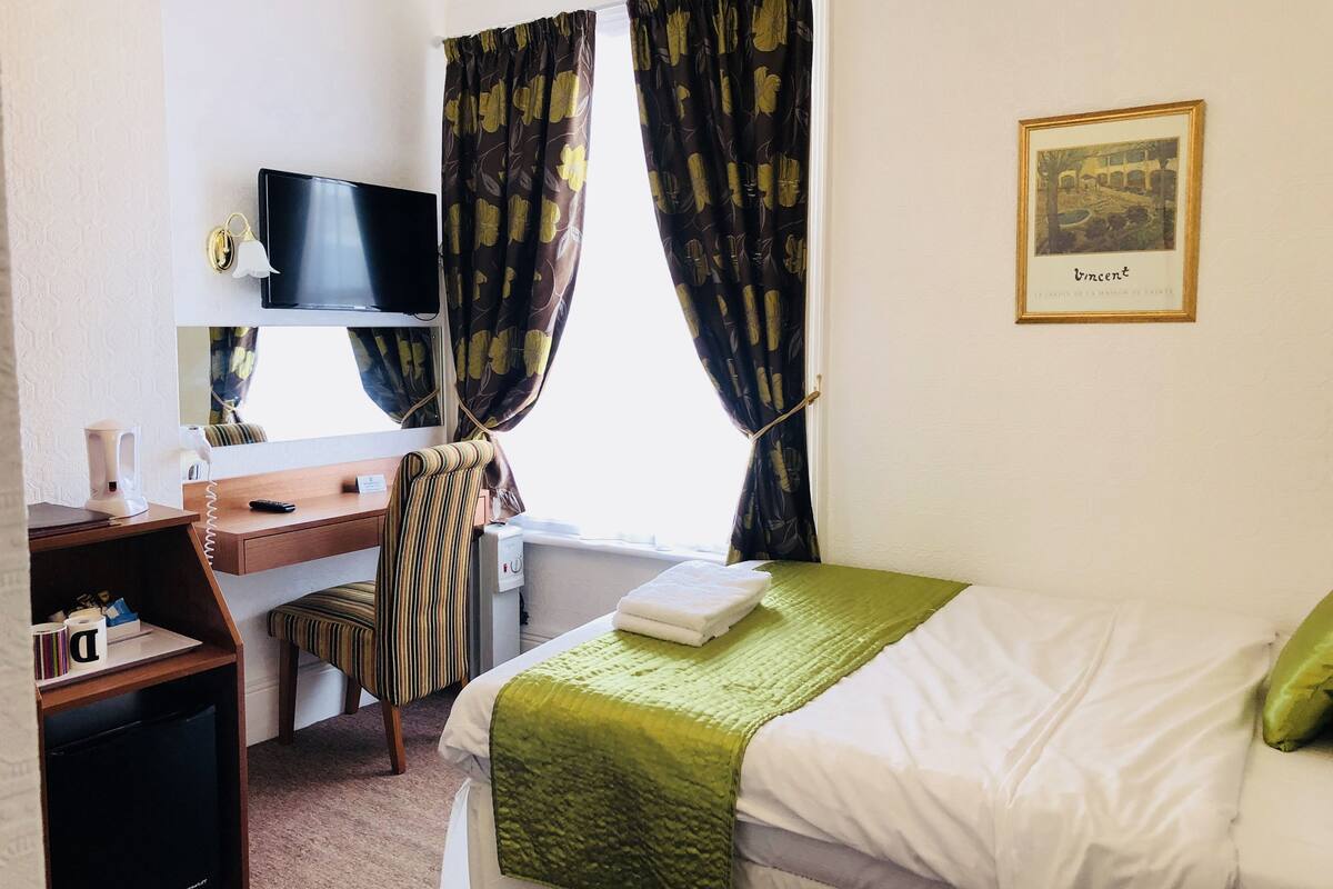 Een hotelkamer met een bed, een bureau met een computer, een stoel, een televisie en een raam met gordijnen.