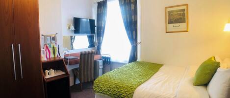 A hotel room with a bed, a desk with a chair, a television, a wardrobe, and a window with curtains.