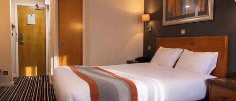 A hotel room with a large bed, a wooden headboard, a nightstand, a lamp, and a framed picture on the wall.