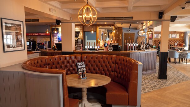 A cozy restaurant with a bar area, a self-serve coffee station, and a seating area with a round table and cushioned bench. - Weathervane Hotel by Greene King Inns (Stoke-on-Trent)