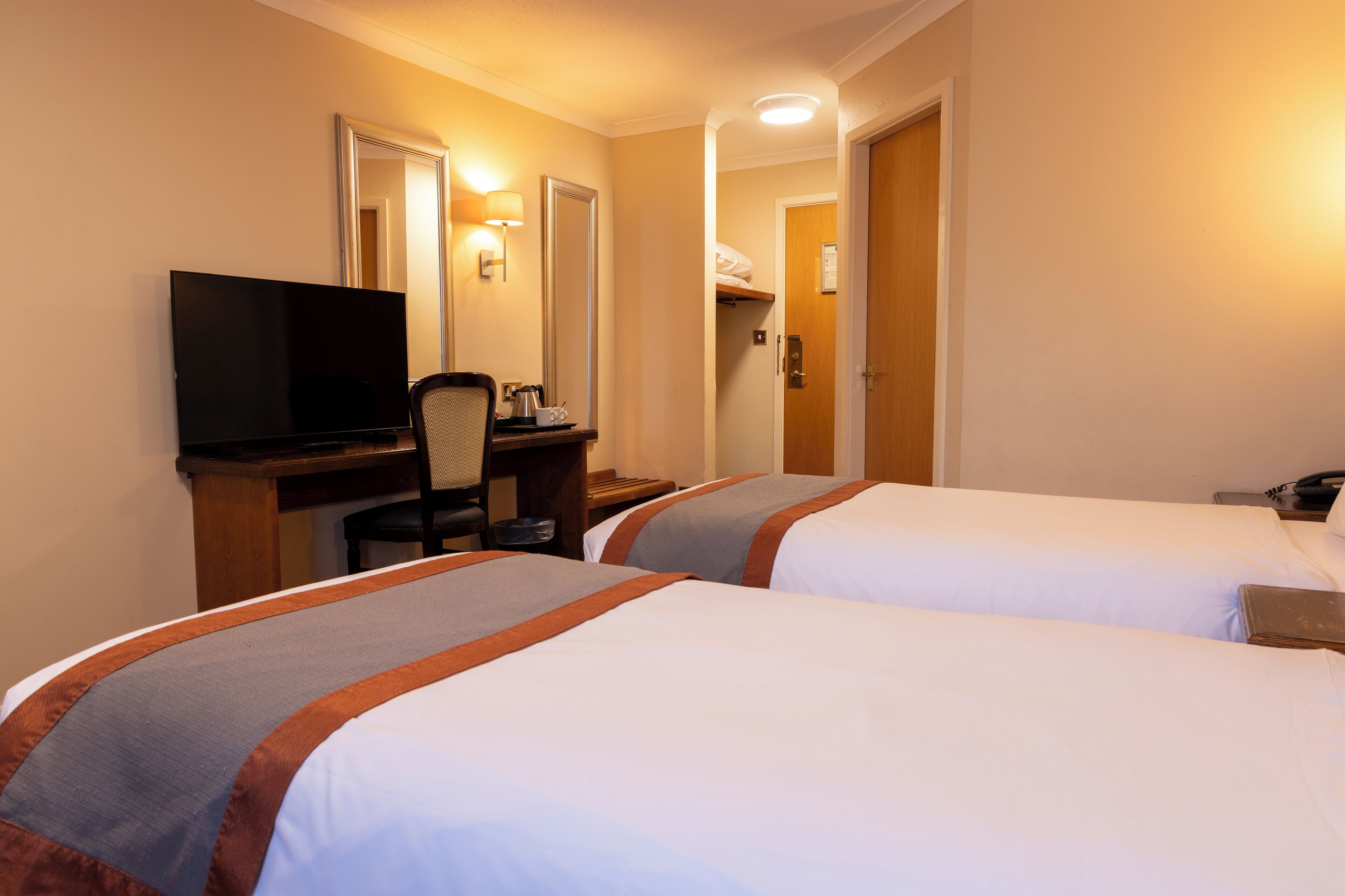 Une chambre d’hôtel avec deux lits, un bureau avec une télévision et une chaise.