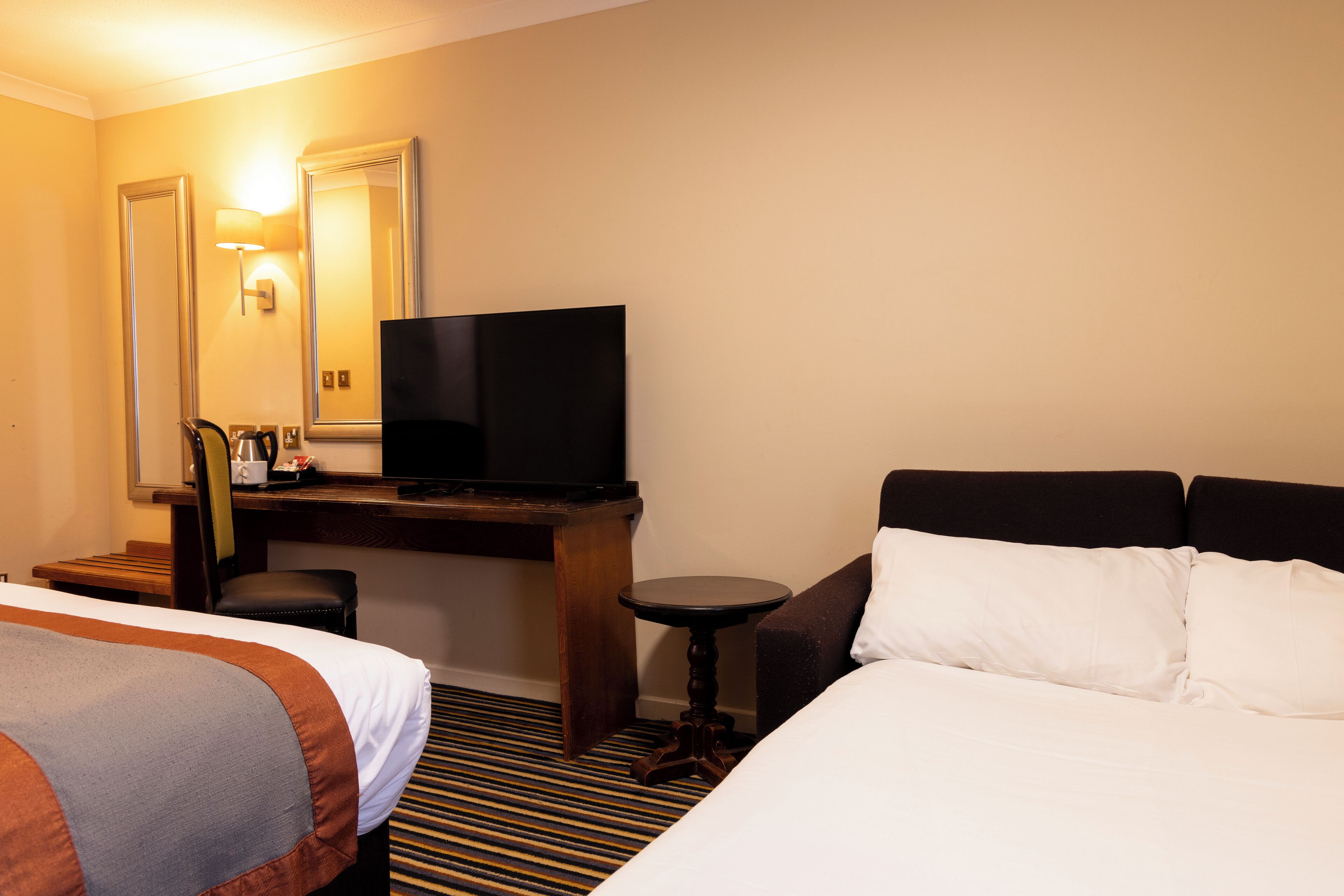 A hotel room with a bed, a desk with a television, a chair, and a small table.