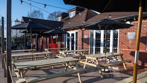 An outdoor seating area with wooden picnic tables and black umbrellas. - Weathervane Hotel by Greene King Inns (Stoke-on-Trent)