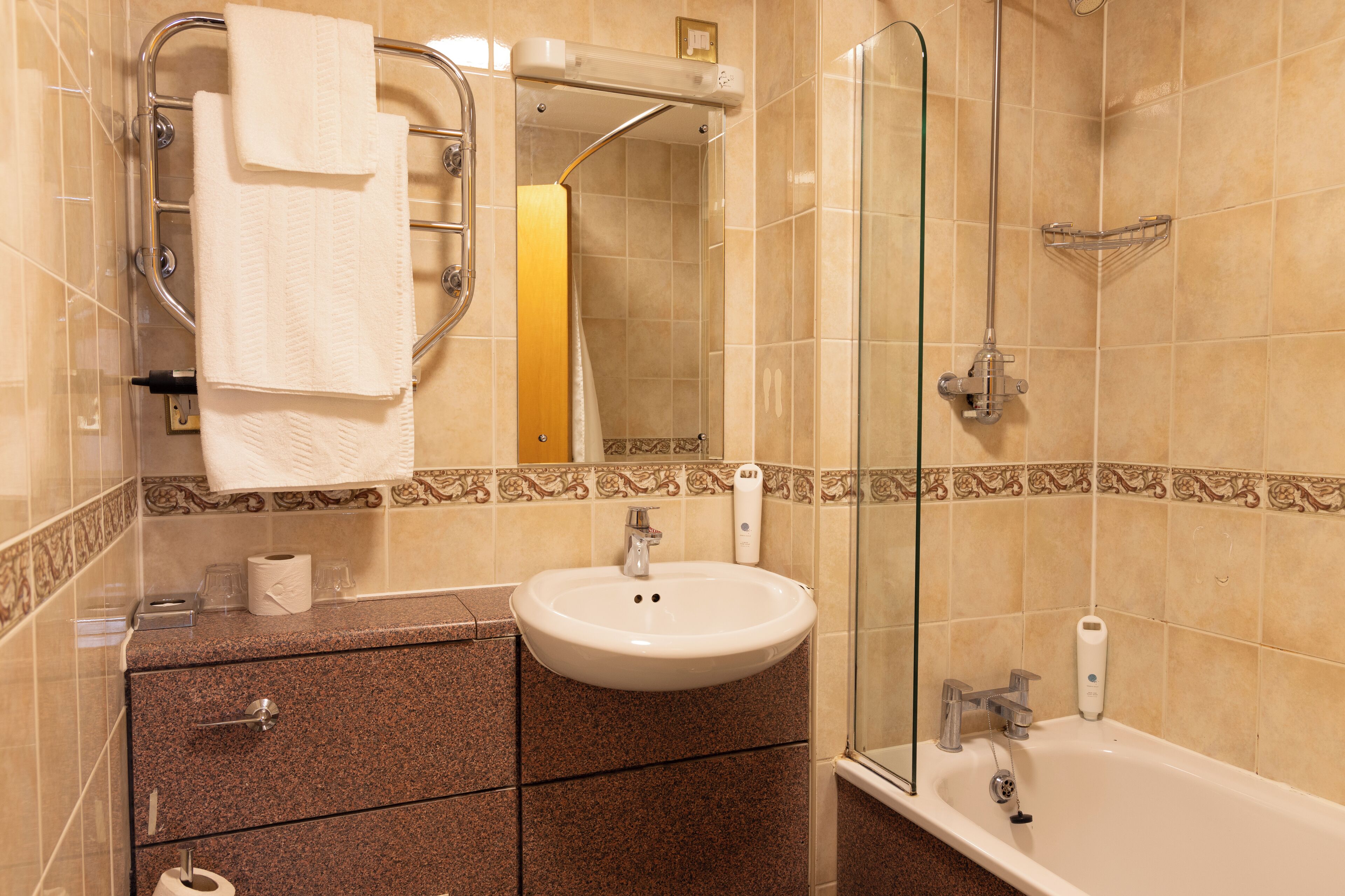 Un baño con lavamanos, espejo, toallero, ducha e inodoro.