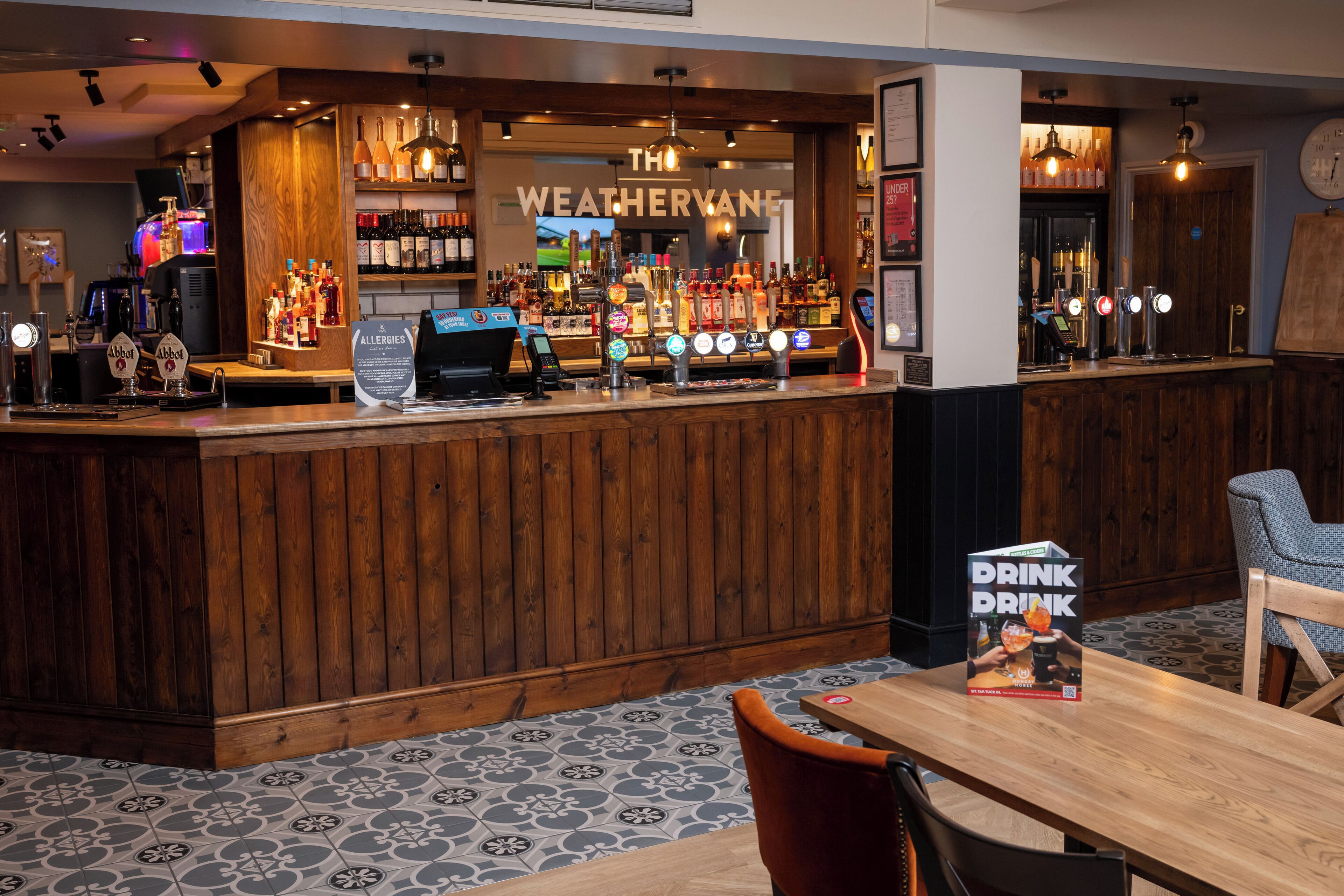 A bar area with a wooden counter, a menu stand, and a seating area with a table and chairs.