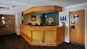 A reception desk with a wooden finish, a clock, and a plant on the wall. - Weathervane Hotel by Greene King Inns (Stoke-on-Trent)