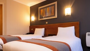 A hotel room with two beds, a wooden headboard, a painting on the wall, and two wall-mounted lights. - Weathervane Hotel by Greene King Inns (Stoke-on-Trent)