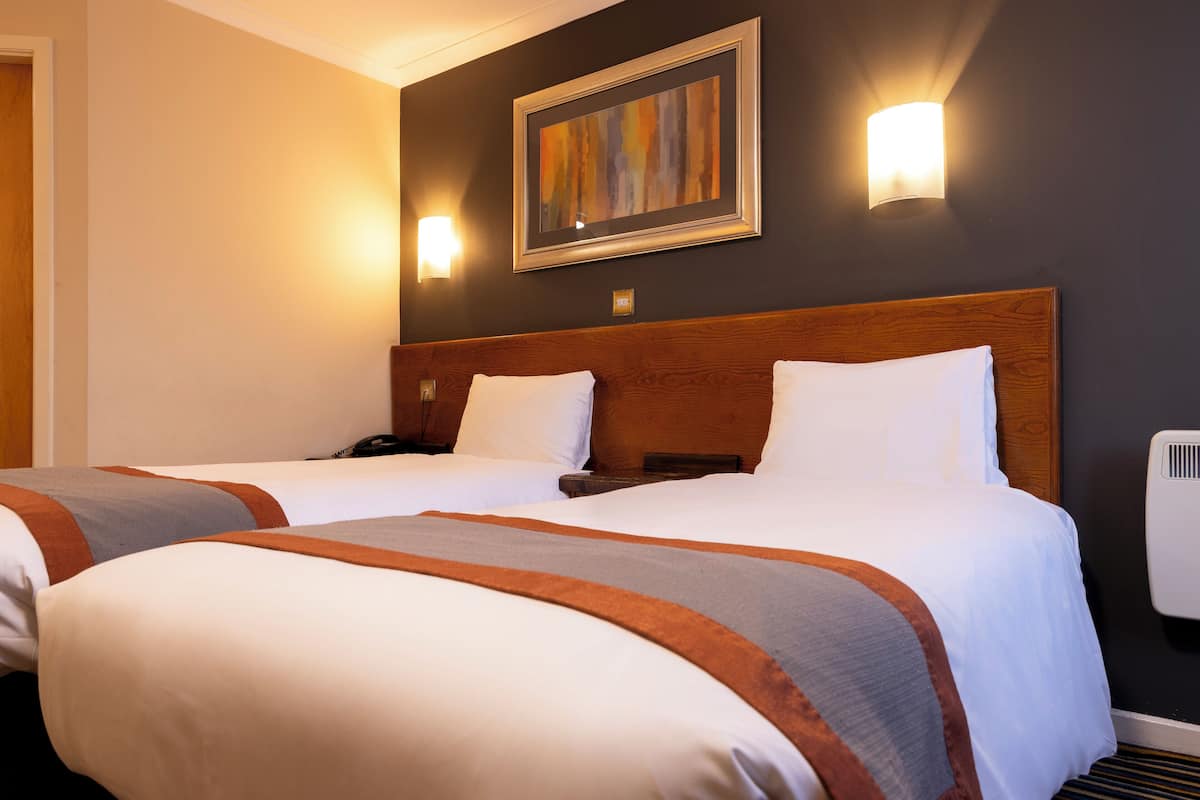Ein Hotelzimmer mit zwei Betten, einem Holzkopfteil, einem Bild an der Wand und zwei Wandlampen.