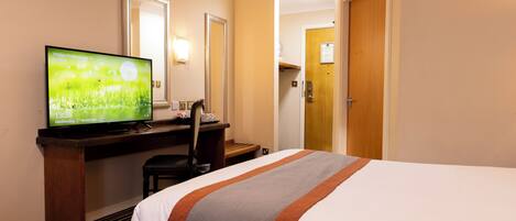 Una habitación de hotel con una cama, un escritorio con un televisor mostrando una pantalla de bienvenida, una silla y una puerta que da a otra habitación.