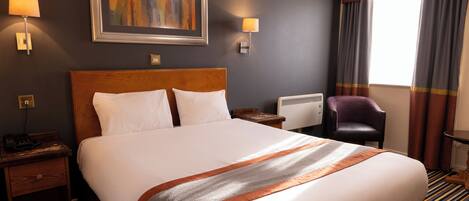 A hotel room with a large bed, two bedside tables, a desk, a chair, and a window with curtains.