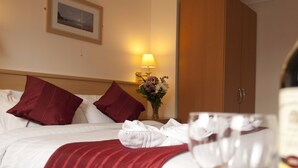A hotel room with a bed, pillows, a bedside lamp, a vase with flowers, and a wine glass. - Denewood Hotel - Guest Accomodation (Bournemouth)