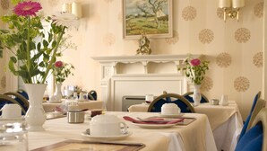 A dining room with tables set for a meal, white tablecloths, and a fireplace. - Denewood Hotel - Guest Accomodation (Bournemouth)