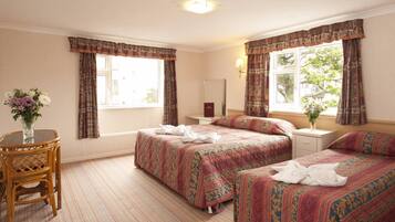 A hotel room with two beds, a bedside table, a chair, and a window with curtains.