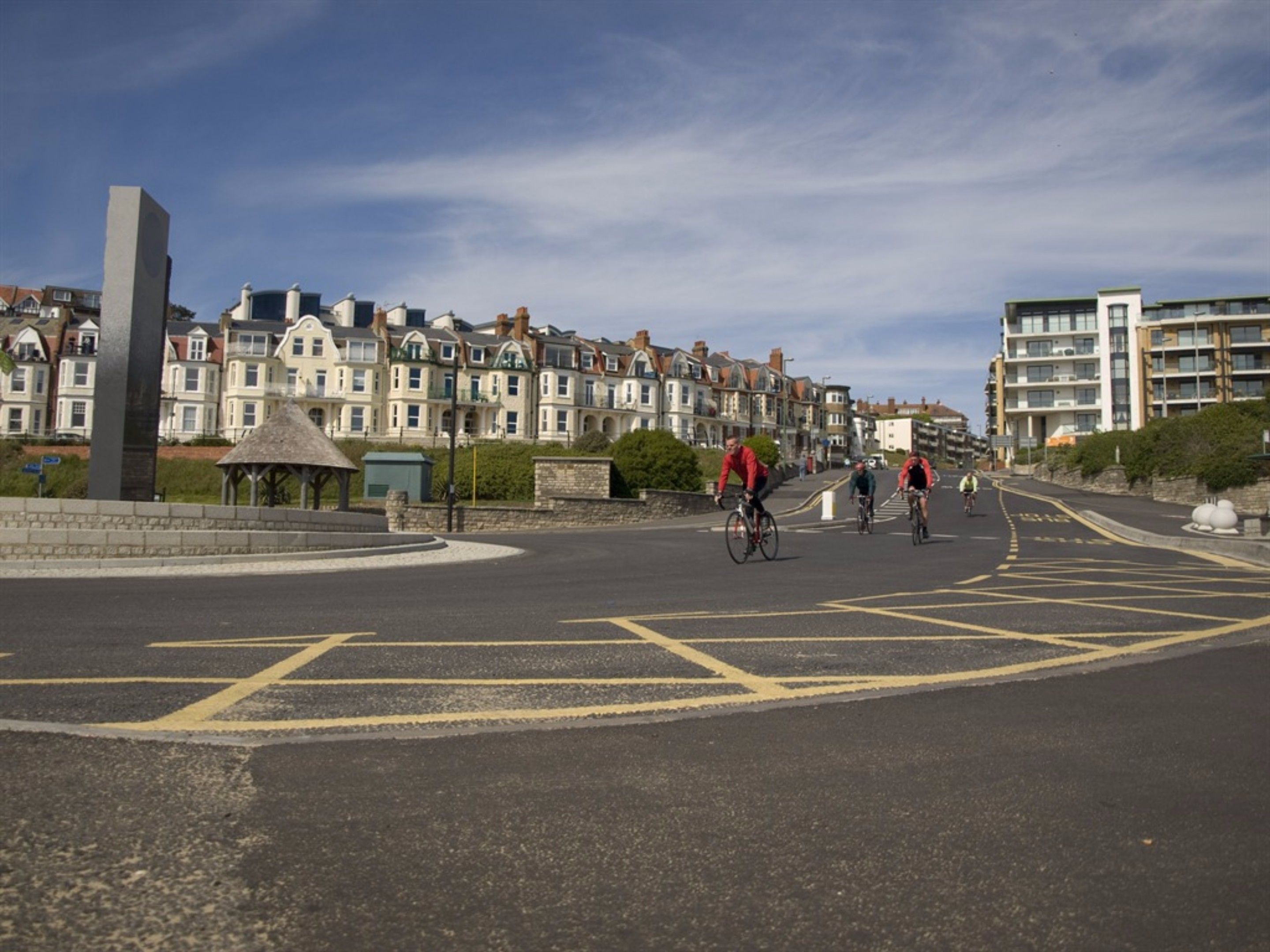 A street with cyclists, a roundabout, and residential buildings.