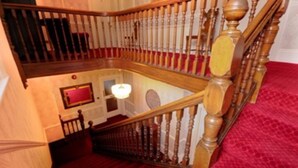 A wooden staircase with a red carpet, a chandelier, and a framed picture on the wall. - Denewood Hotel - Guest Accomodation (Bournemouth)