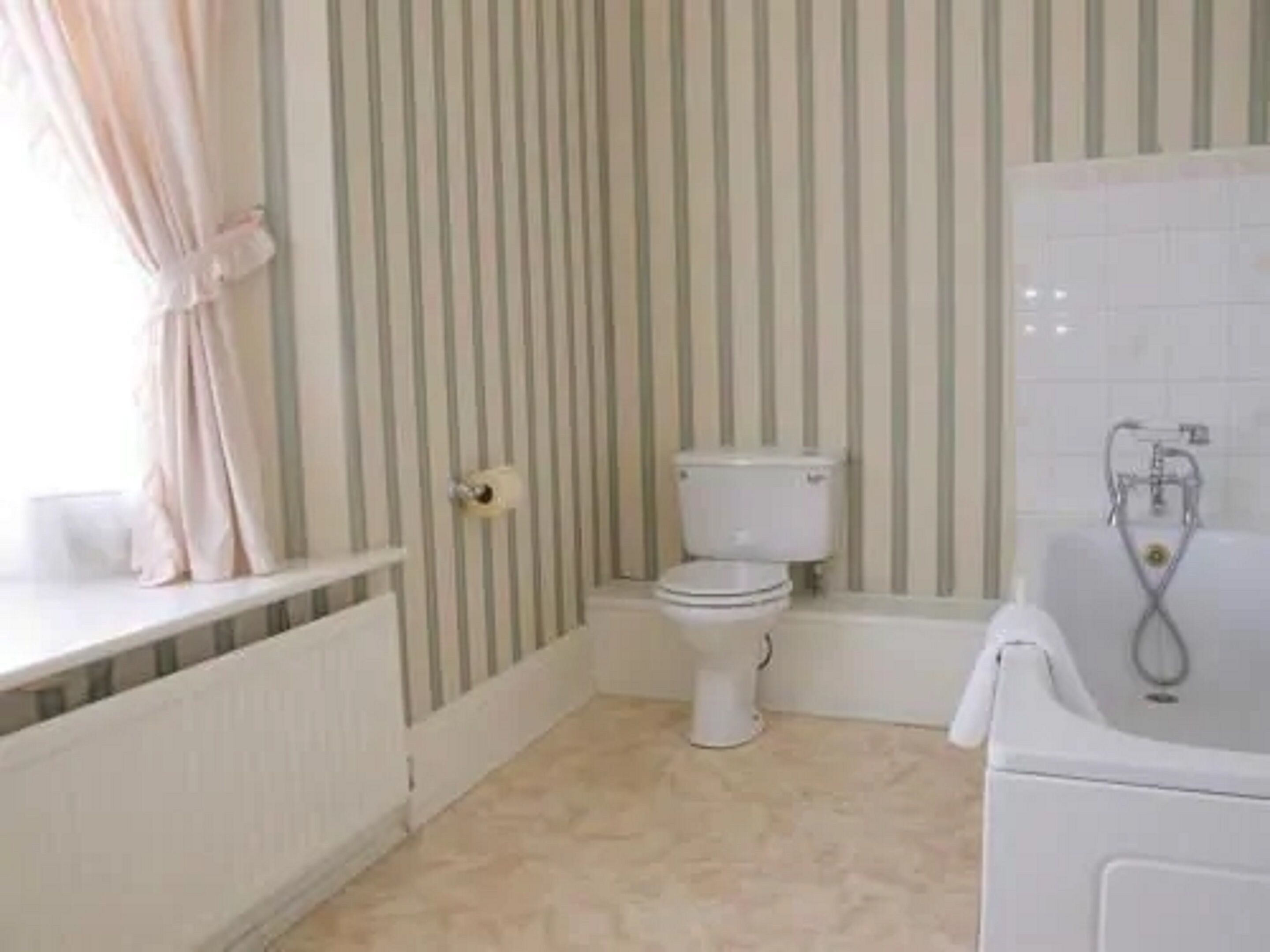 Un baño con inodoro, bañera y ventana con cortinas.