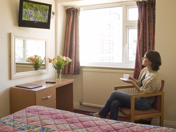 Un dormitorio con una cama, un escritorio, una silla, un televisor y una ventana con cortinas.