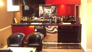 A bar area with a counter, two black leather chairs, and a red and black color scheme. - The Mayfair Hotel (Bournemouth)