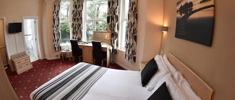 Habitación de hotel con una cama grande, un escritorio y una silla. Hay un televisor en la pared y una ventana con cortinas.