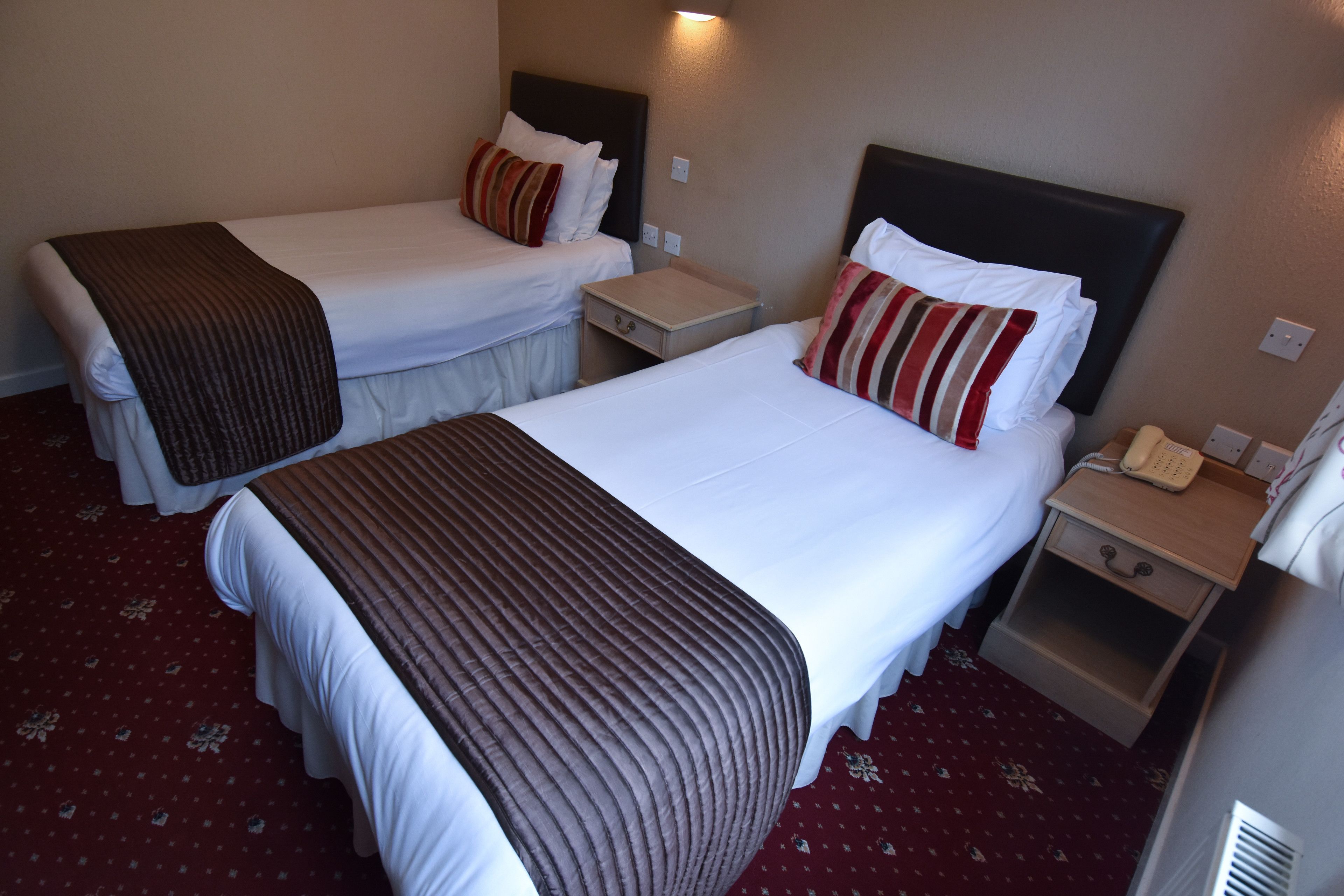 A hotel room with two beds, each with a headboard, bedside tables, and a telephone on one of the tables.