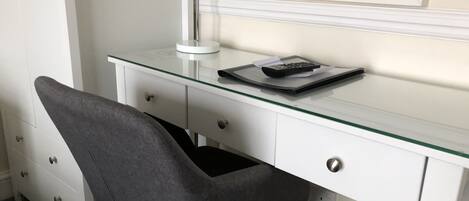 A white desk with a glass top, a grey chair, a desk lamp, and a keyboard.