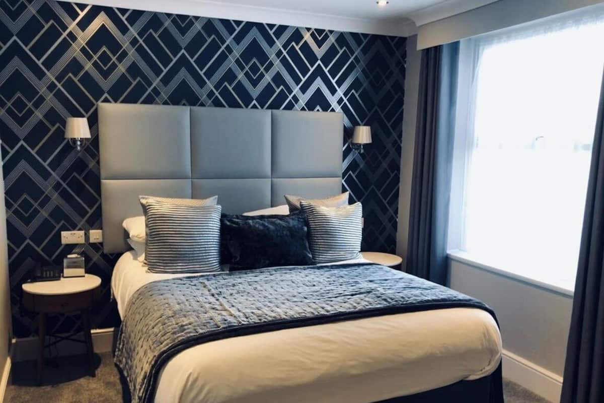 Una habitación de hotel moderna con una cama grande, un cabecero y una mesita de noche con lámpara.