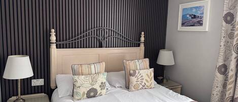 A neatly made bed with striped bedding, two bedside tables with lamps, a wall-mounted picture, and a curtain with a floral pattern.