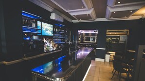 A bar area with a long counter, shelves with bottles, and a television screen. - Camelia Hotel (Southend-on-Sea)