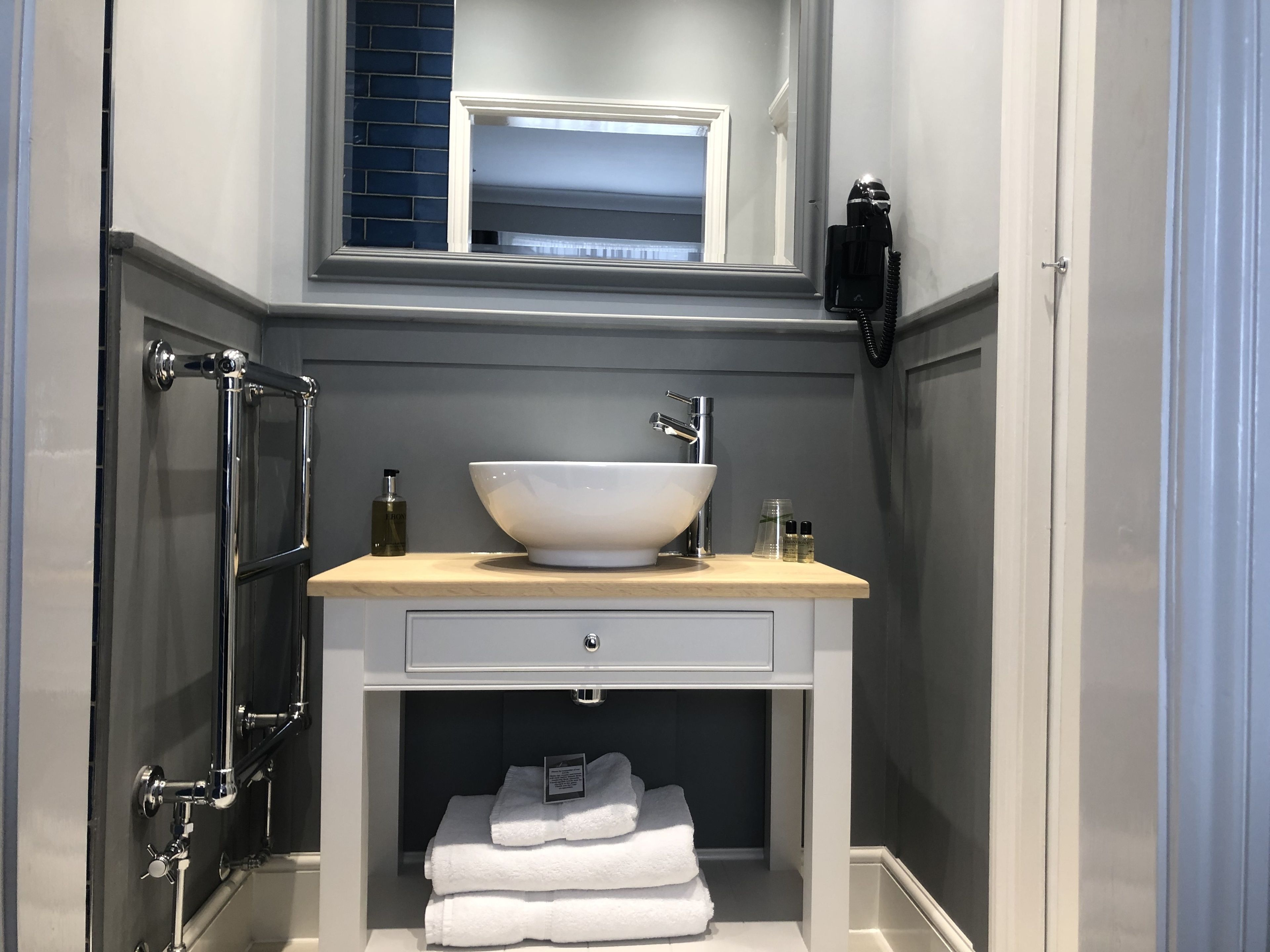 A bathroom with a white sink, a mirror above it, a towel rack, and a shower area.