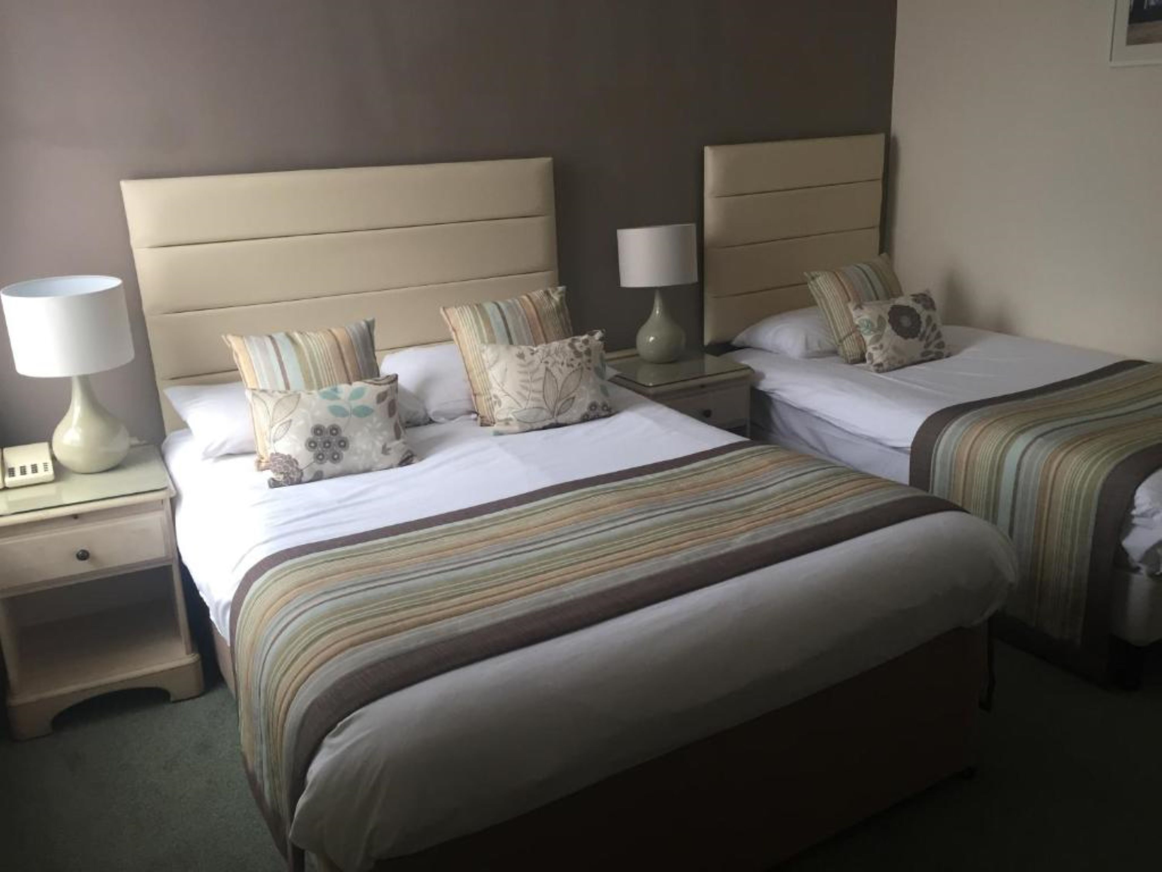 A hotel room with two beds, each with a striped bedspread, a nightstand with a lamp, and a wall-mounted lamp.