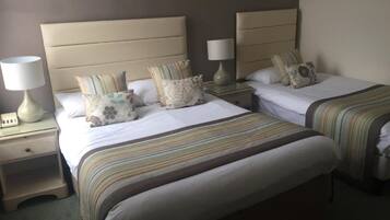 A hotel room with two beds, each with a striped bedspread, a nightstand with a lamp, and a wall-mounted lamp.