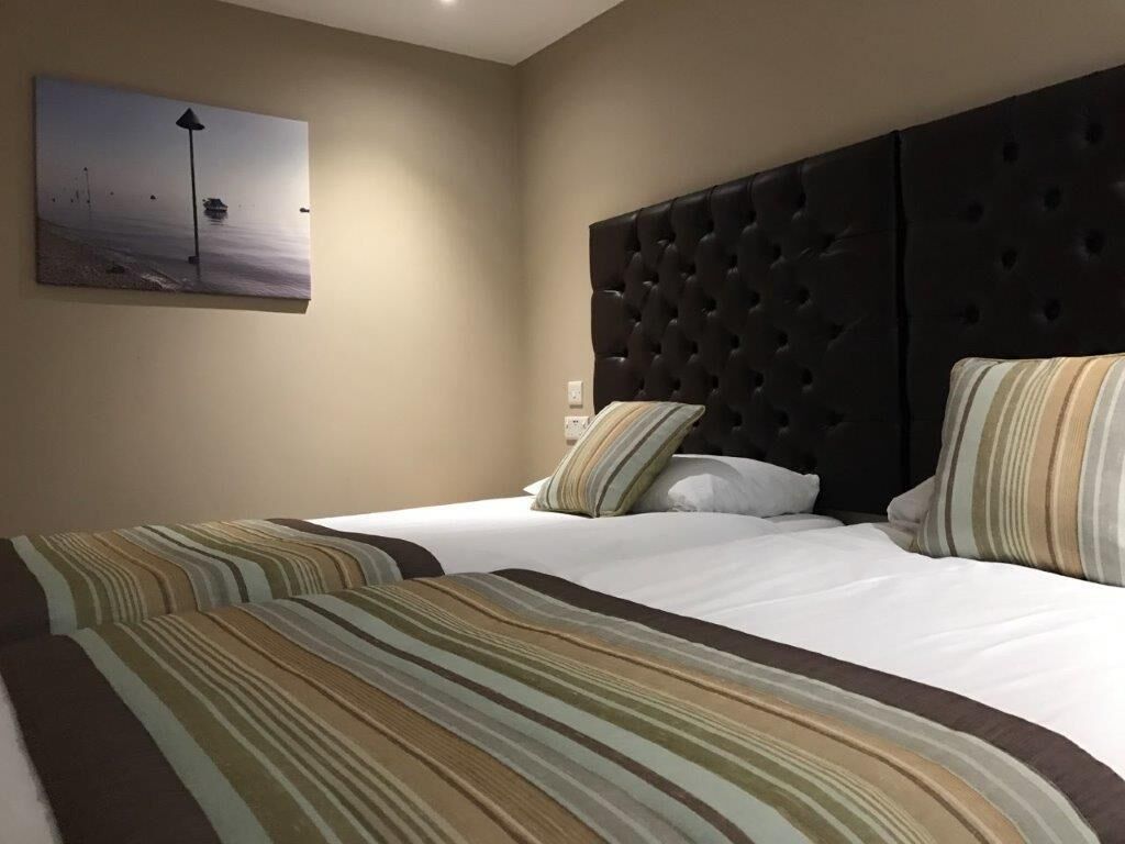 A hotel room with two beds, striped bedding, a dark headboard, and a painting of a beach scene.