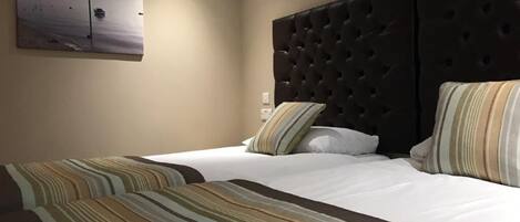 A hotel room with two beds, striped bedding, a dark headboard, and a painting of a beach scene.