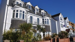 A row of white buildings with balconies, a brick wall, and some greenery in front. - Camelia Hotel (Southend-on-Sea)
