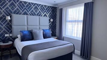 A modern hotel room with a large bed, a headboard, two bedside tables, and a window with curtains.