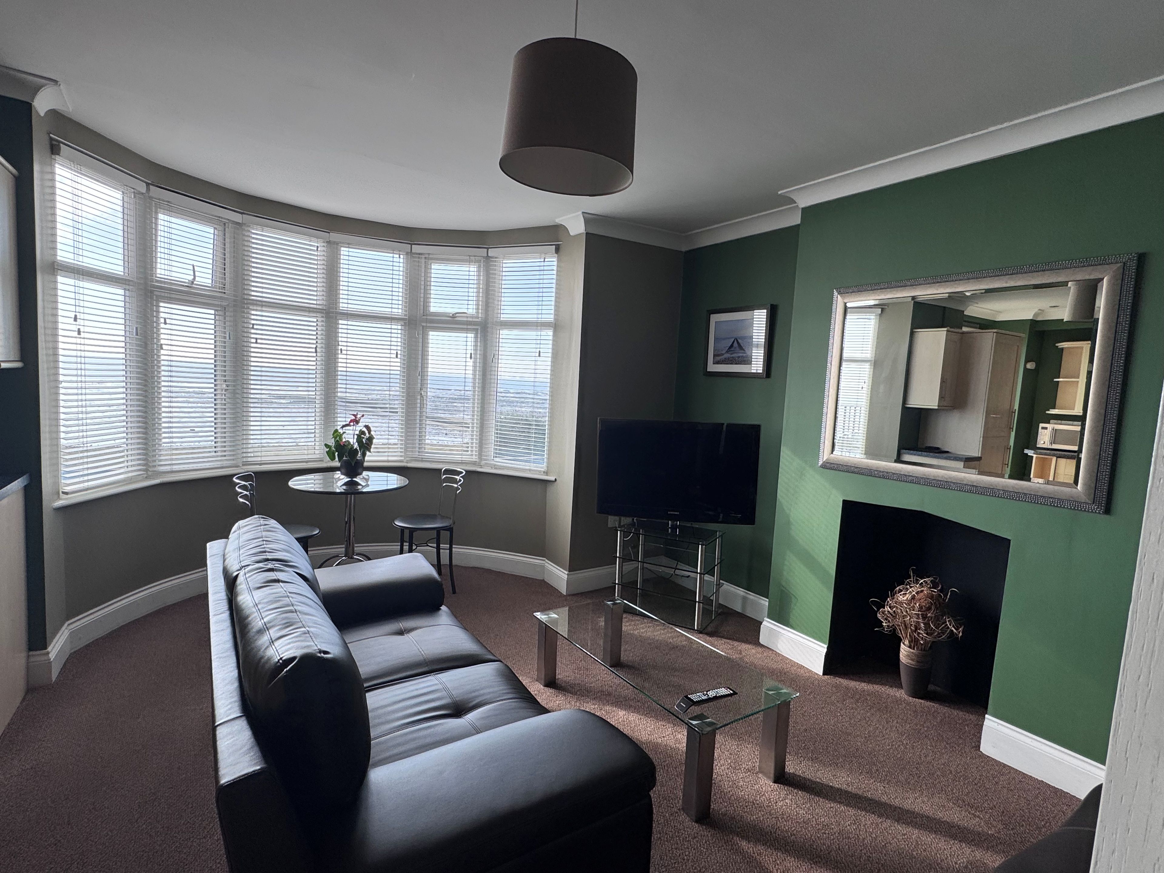 A modern living room with a sofa, a TV, a fireplace, and large windows.