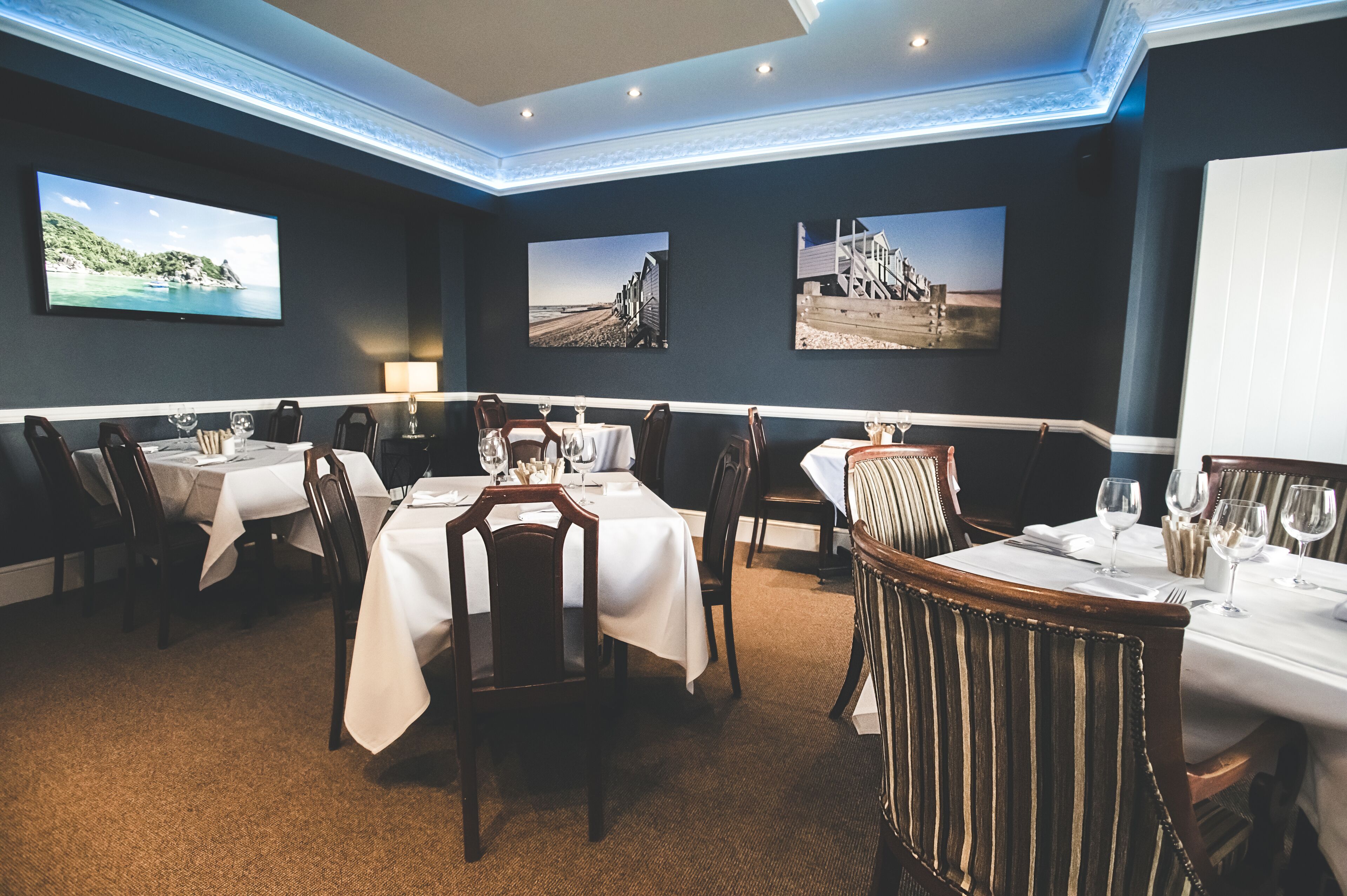 A dining area with tables set for four, each with white tablecloths and wooden chairs.