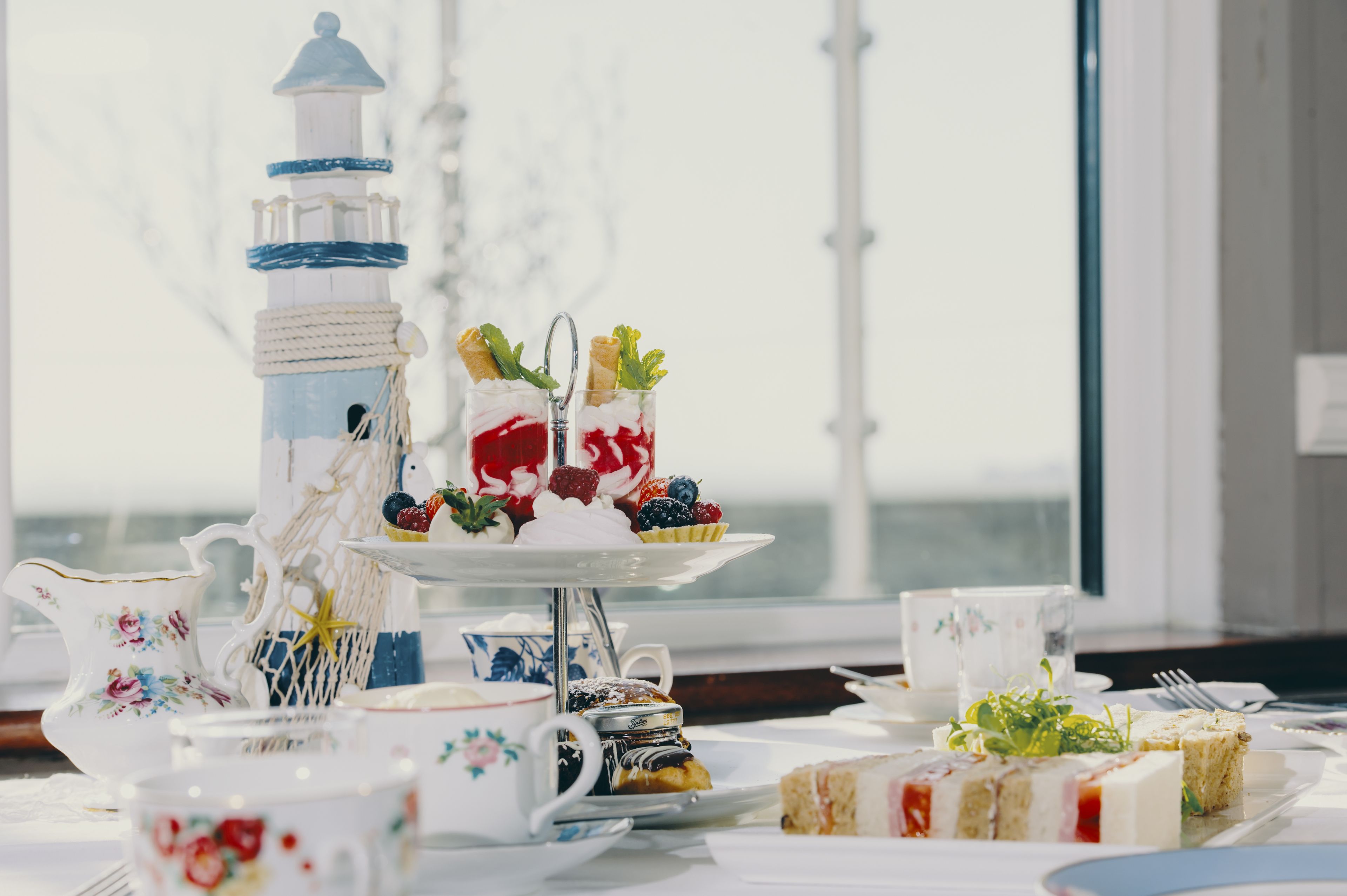 A three-tiered tea service with pastries and fruits, a decorative lighthouse, and floral-patterned tableware.
